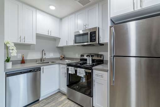 Two Bedroom Apartments in Hayward CA - Paseo Gardens - Modern Kitchen with Grey Countertops, White Cabinetry, Stainless Steel Appliances, and Wood Flooring