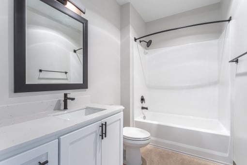 a bathroom with white fixtures and a white toilet next to a white bathtub with a shower