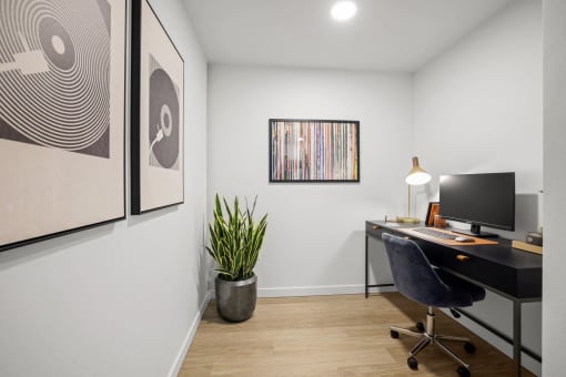 a home office with a desk and a monitor and a plant