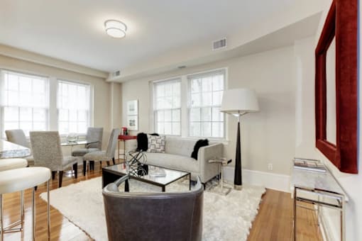 A living room with a grey couch, a white rug, and a red picture frame on the wall.