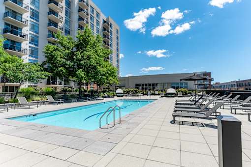 A swimming pool surrounded by lounge chairs and trees in front of a building.