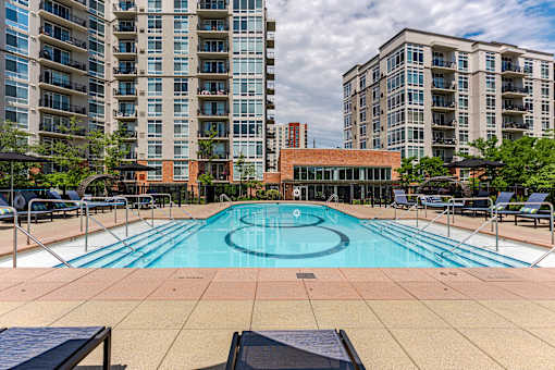 A large outdoor swimming pool with lounge chairs and apartment buildings in the background.