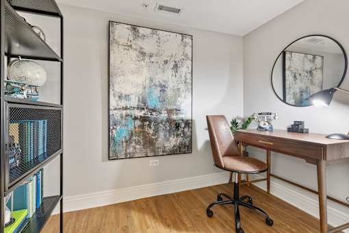 A room with a desk, chair, and a painting on the wall.
