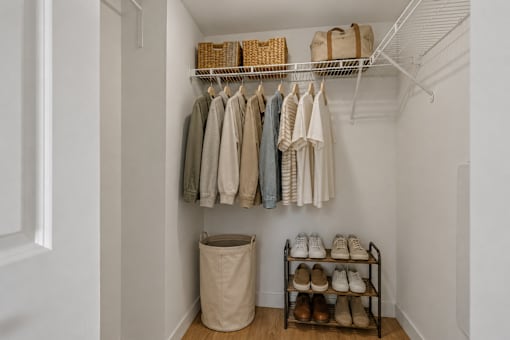 A white closet with clothes hanging and shoes on a shelf.