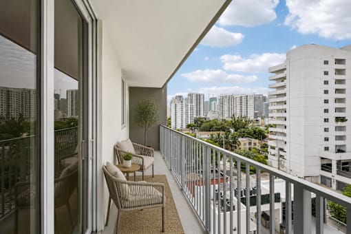 A balcony with a table and chairs overlooks a cityscape.