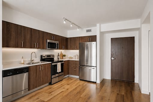 Modern kitchen with stainless steel appliances, quartz countertops, and wood-style cabinetry inside a one-bedroom apartment at Riverview One Apartments in Downtown Miami.