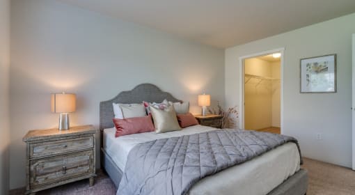 Apartments For Rent In Coeur d'Alene, ID - Rockwood Lodge - Bedroom With Carpeted Flooring, Large Bed, Wooden Nightstands With Lamps, And Spacious Closet.