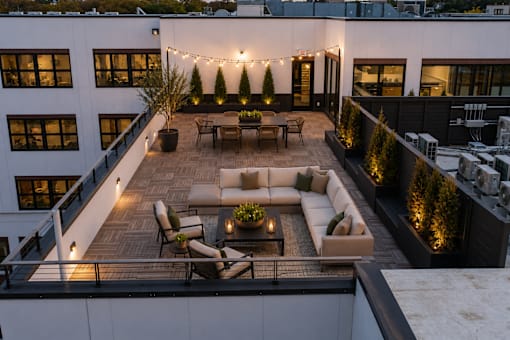 A rooftop patio with a couch, chairs, and string lights.