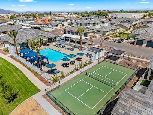 A tennis court is surrounded by a pool and palm trees.
