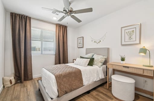 A bedroom with a bed, desk, and window with curtains.