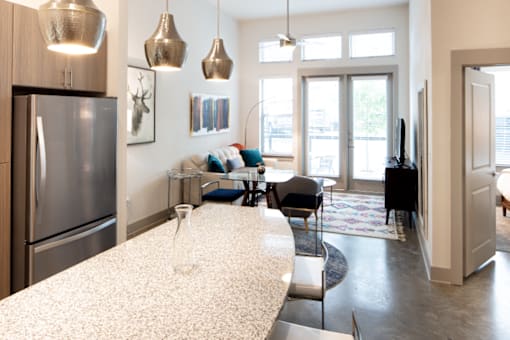 A modern kitchen with a refrigerator, a dining table with chairs, and pendant lights hanging from the ceiling.