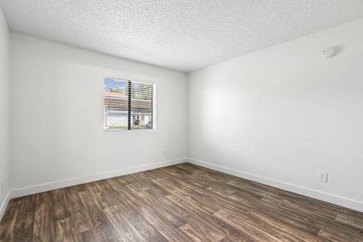 A room with wooden flooring and a window showing a view of a building.