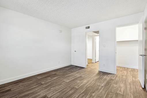 A room with white walls and wood flooring with a doorway leading to another room.