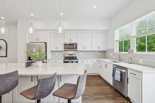 A kitchen with white cabinets and a large island with chairs.