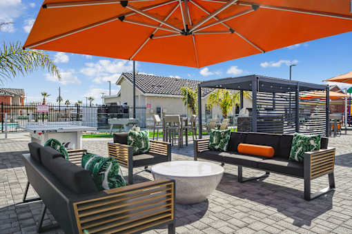 A patio with a table, chairs and a bench under an orange umbrella.