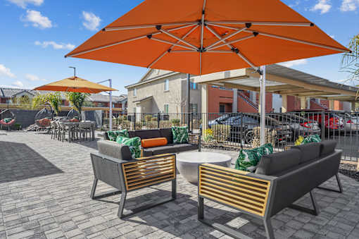 Two chairs and a table are under an orange umbrella.