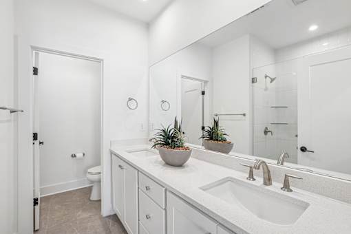 A white bathroom with a sink, mirror, and potted plants.