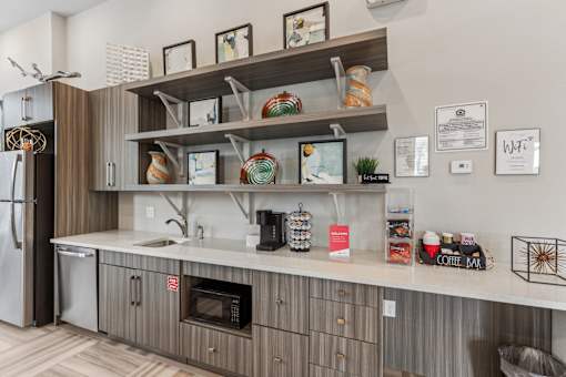 A kitchen with a refrigerator, microwave, and shelves with various items.