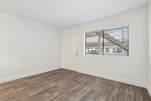 A room with a wooden floor and a window showing a building outside.