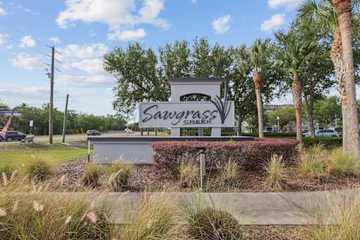 A sign that says Sawgrass in front of some trees.
