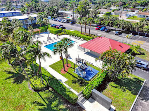 A red-roofed building is surrounded by a green lawn and a pool.