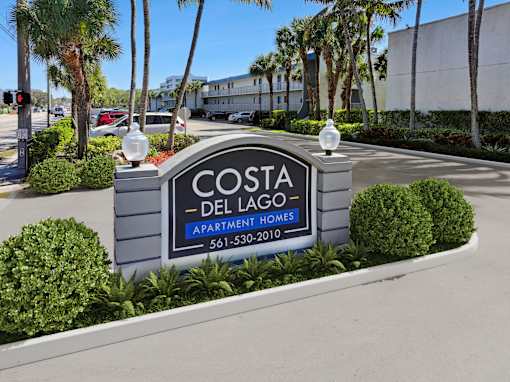 A sign for Costa Del Lago Apartments is in front of a building and some trees.