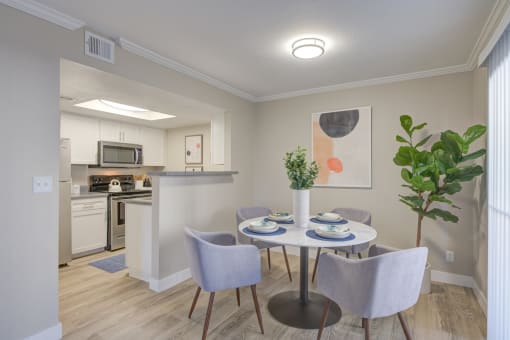 Two-Bedroom Apartments in Moreno Valley, CA - Ardella on Chagall - Dining Area with Hardwood-Style Flooring, Round Table and Four Chairs, Houseplant, and View of Kitchen.