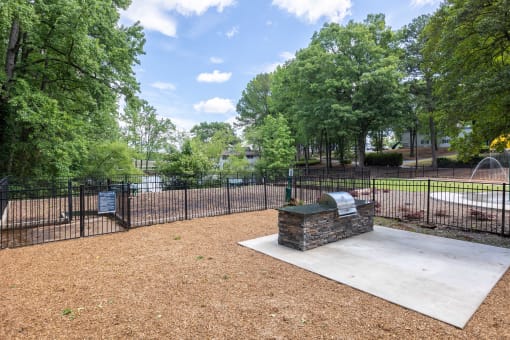 a fenced in dog park with a fountain and trees
