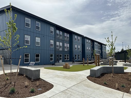 A modern building with a blue exterior and a courtyard with concrete benches and trees.