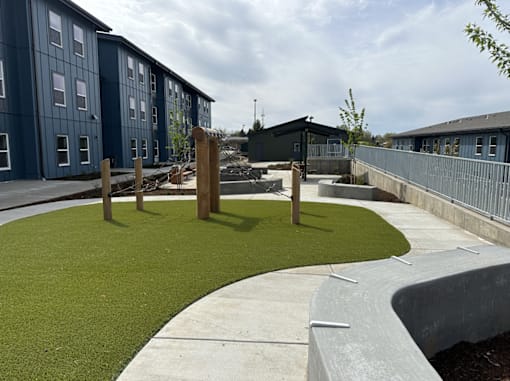 A playground area with artificial grass and a wooden structure in the middle.