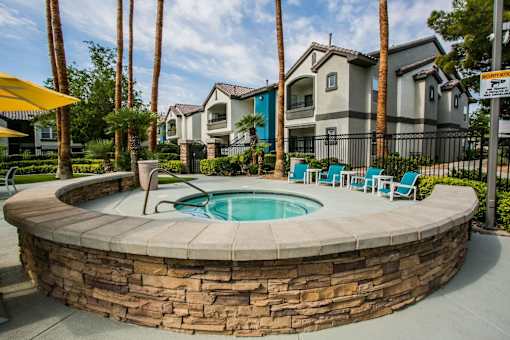 A pool surrounded by a stone wall with chairs and palm trees.