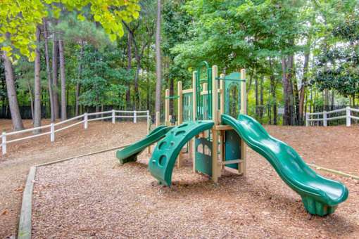 A green slide in a playground surrounded by trees.