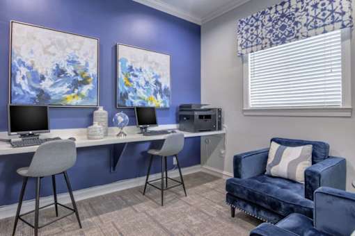 A room with a blue couch, a desk with a computer, and two chairs.