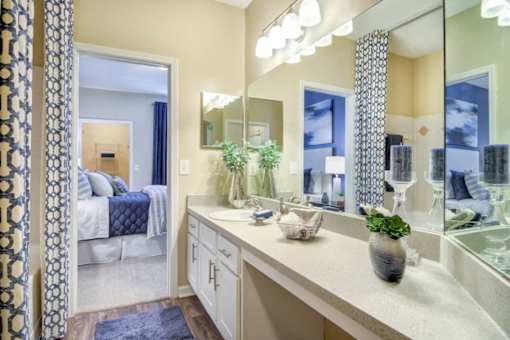 A bathroom with a large mirror, a sink, and a bedroom visible through the door.