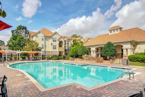 Pet-Friendly Apartments in Duluth– Grande Club – A large swimming pool in front of a building with a patio and umbrellas.