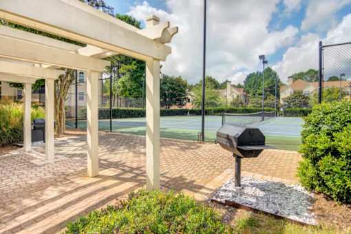 A tennis court is surrounded by a white pergola and a mailbox.