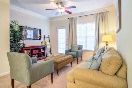 A living room with a green chair, a brown ottoman, and a yellow couch.