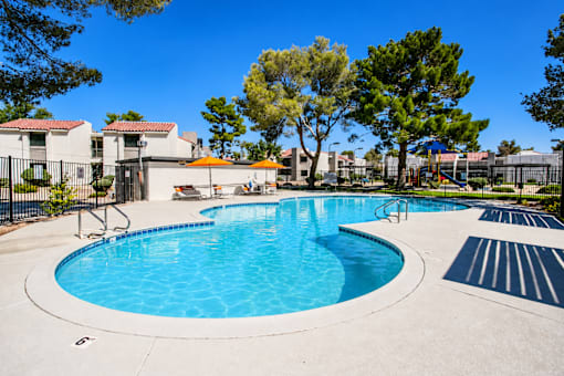 Outdoor swimming pool surrounded by mature trees at Haven at Lone Mountain apartments in Las Vegas
