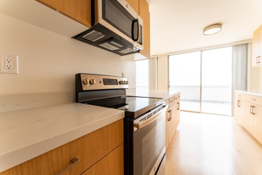 Santa Monica, CA Apartments near Dodger Stadium - San Vicente Tower - Modern Kitchen with Wood-Style Cabinetry, White Quartz Countertops, with a Stainless Steel Microwave, a Stove, and an Oven