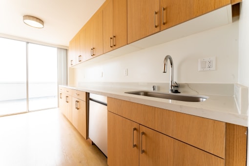 Apartments for Rent in Santa Monica, CA - San Vicente Tower - Kitchen with Wood Cabinets, Stainless Steel Appliances, Hardwood Flooring, Large Sliding Glass Door, and White Countertops