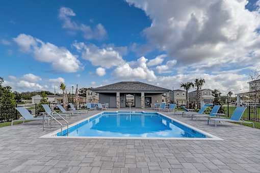 A swimming pool surrounded by a stone patio and lounge chairs.