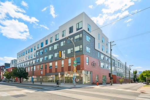 A modern multi-story building with a mix of red and grey facade stands on a street corner.