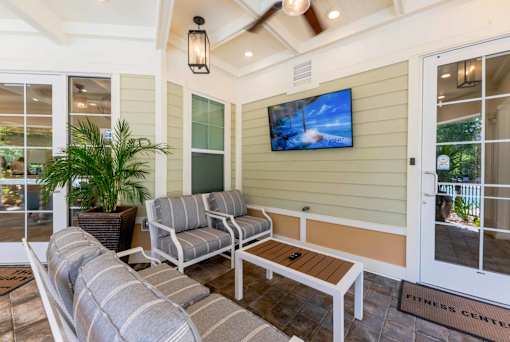 A patio with a couch, chair, and a television on the wall.