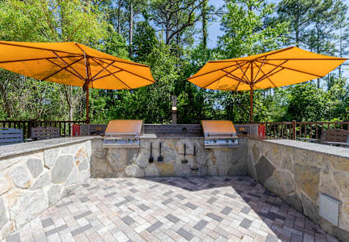 Outdoor grilling stations with umbrellas at The Sanctuary at 331 apartment complex in Santa Rosa Beach, Florida, surrounded by seating areas.