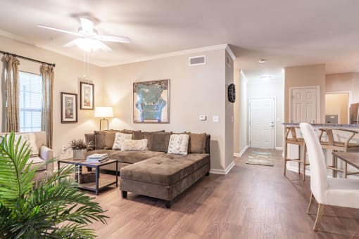 Opelika, AL Apartments – The Crossings of Opelika - a living room with a couch and a table with hardwood floors and a ceiling fan