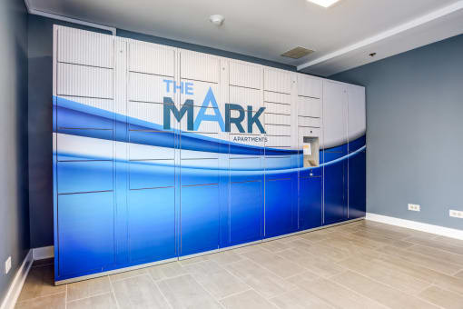 Glendale Heights Apartments - package locker storage room with blue and white painted doors and a large property logo for The Mark
