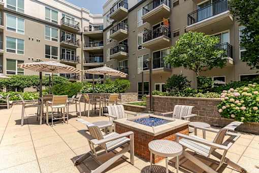 A patio area with chairs and tables is surrounded by apartment buildings.