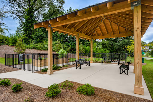 A wooden pavilion with a black fence and benches in front.