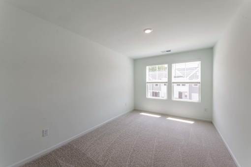 Carpeted bedroom with two windows, neutral walls, and natural light at Townes at Olde Birch townhomes in Raleigh, NC.