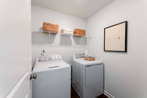 In-home laundry room with full-size washer and dryer, wall shelving, and storage space at Townes at Olde Birch townhomes in Raleigh, NC.